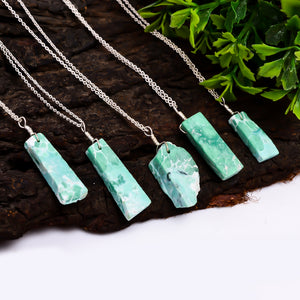 Raw variscite gemstone pendant necklaces arranged outdoors on a natural background showing green hues and irregular bar shapes
