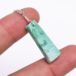 Close-up of a natural green variscite raw stone pendant held in hand highlighting its unique bar shape and healing crystal texture