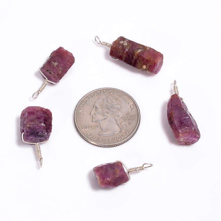 Raw ruby crystal bar pendants shown with a coin for size reference highlighting natural pink color and AA+ quality texture