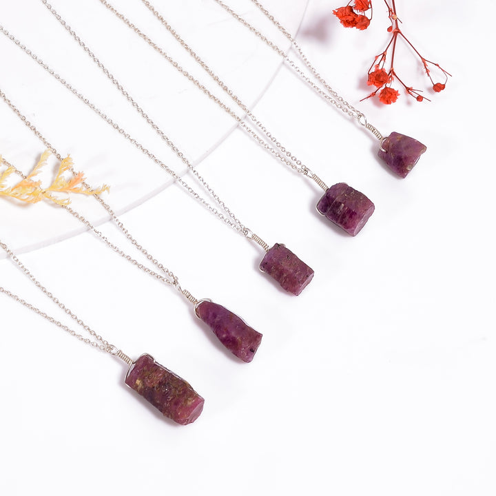 Natural raw ruby crystal bar pendant necklaces arranged on silver-plated chains in a flat lay style with pink gemstones