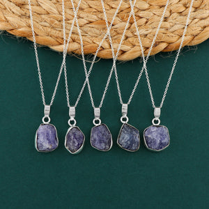 Real tanzanite raw stone pendant held in hand showing natural blue color, bezel frame and silver-plated chain details