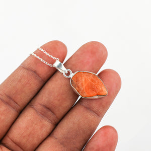 Close-up of natural triplite raw crystal pendant held in hand showing rough cut, bezel setting and bright orange gemstone color