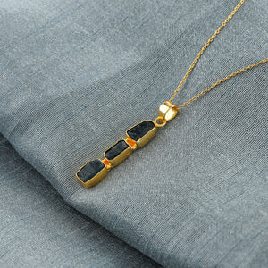 Close-up view of natural sapphire raw gemstone pendant with irregular cut set in gold bezel on 18-inch chain