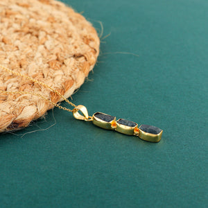 Natural blue sapphire raw stone pendant held in hand showing irregular shape and gold-plated setting on delicate chain