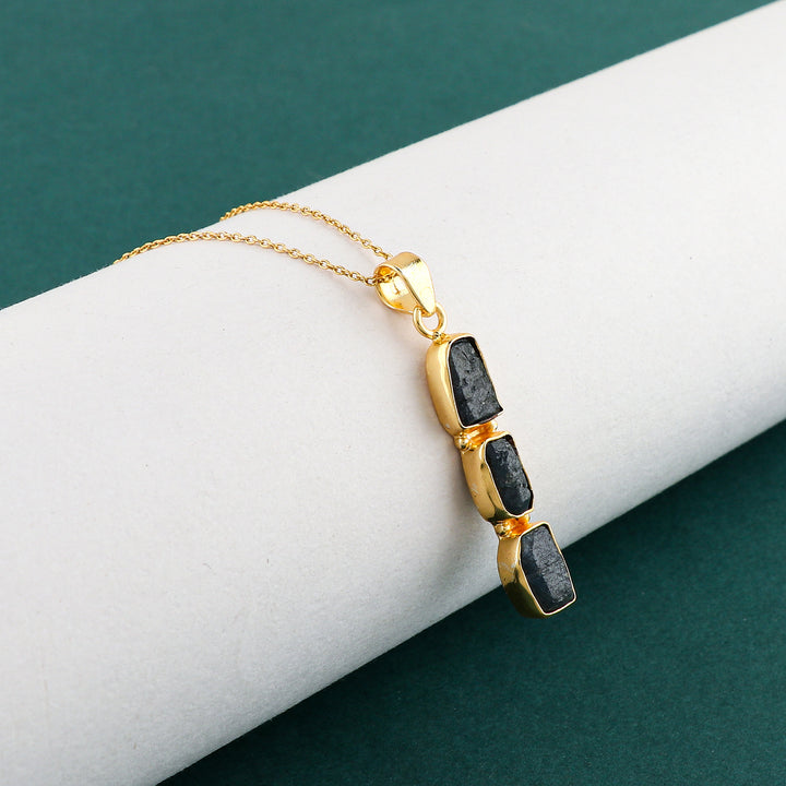 Raw sapphire crystal pendant necklace shown on white background highlighting deep blue color and dainty gold-plated bezel setting