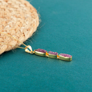 Ruby raw crystal pendant necklace placed on soft fabric highlighting pink hue and elegant gold-plated finish