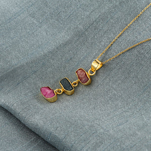 Natural sapphire and ruby raw crystal pendant necklaces arranged in a row with blue and pink stones in gold-plated bezels on 18-inch chain