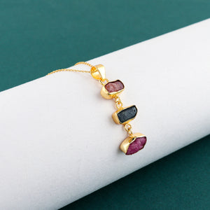 Close-up of natural sapphire and ruby raw gemstone pendant with irregular cuts set in gold-plated bezel on 18-inch chain