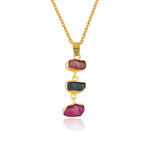 Raw sapphire and ruby crystal pendant necklace in gold-plated bezel displayed on white background showing vibrant blue and pink gemstones