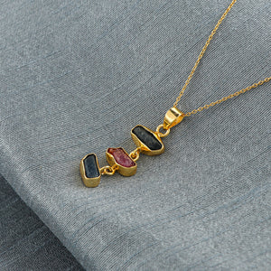 Sapphire and ruby raw crystal pendant necklace placed on soft fabric showing rich blue and pink hues with gold-plated setting