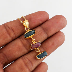 Natural sapphire and ruby rough stone pendant held in hand highlighting irregular shapes, dual gemstones and gold-plated bezel on 18-inch chain