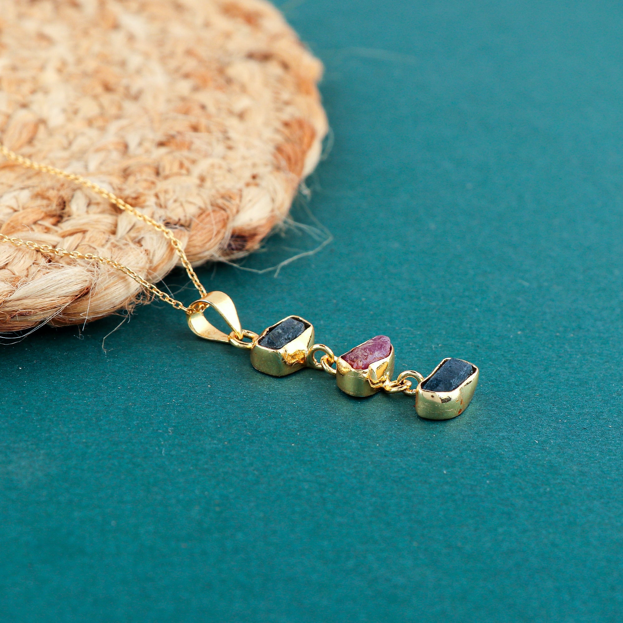 Natural sapphire and ruby rough crystal pendant necklaces arranged in a row with blue and pink raw gemstones in gold-plated bezels on 18-inch chains
