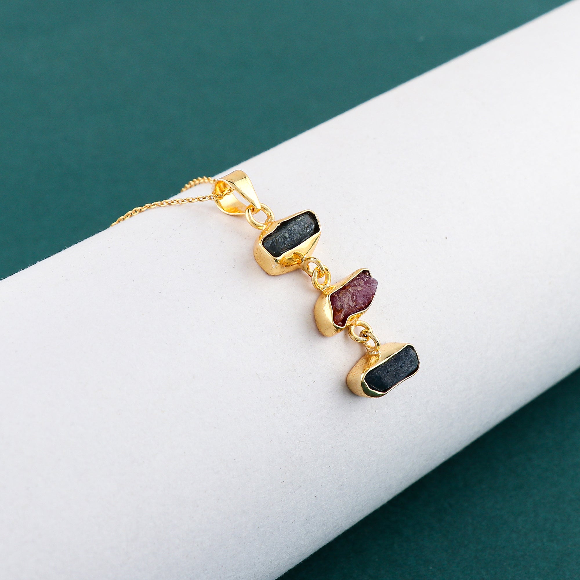 Close-up of natural sapphire and ruby rough gemstone pendant with irregular cuts set in gold-plated bezel on delicate 18-inch chain