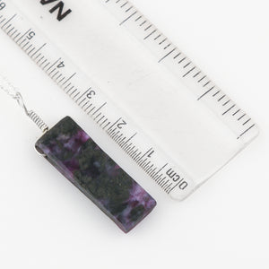 Rectangular purple and black patterned pendant with a ruler for scale on a white background
