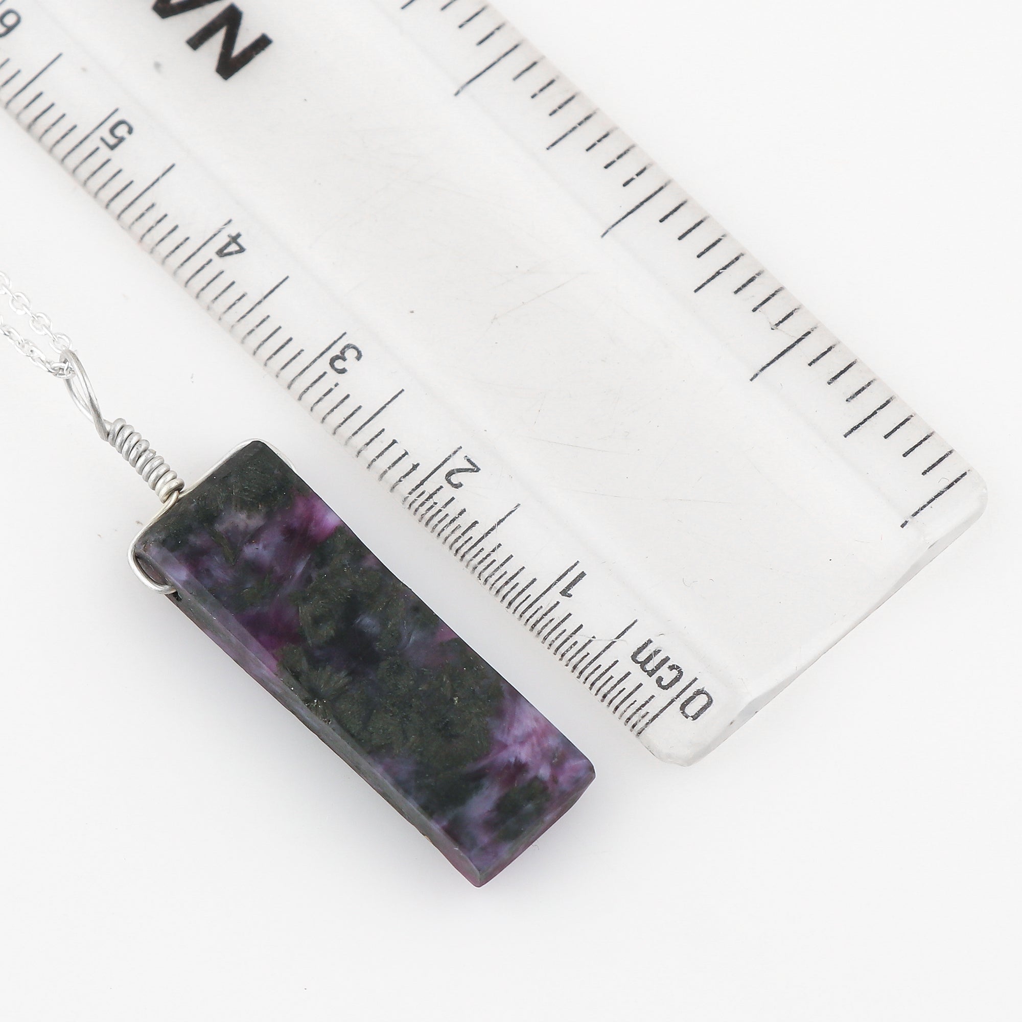 Rectangular purple and black patterned pendant with a ruler for scale on a white background