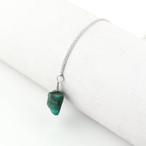 Natural raw emerald crystal pendant necklaces arranged in a row showing vibrant green irregular stones on silver-plated 18-inch chains